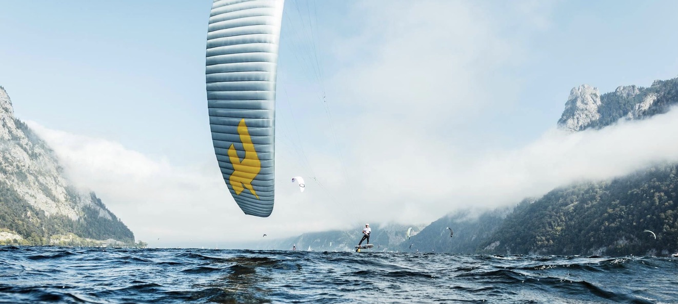 A foil kite swooping low over a kitefoiler racing on a mountain lake