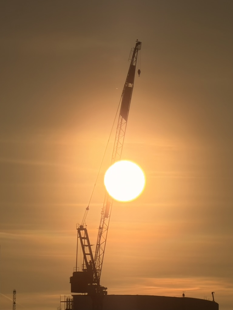 The sun setting behind silhouetted harbour cranes