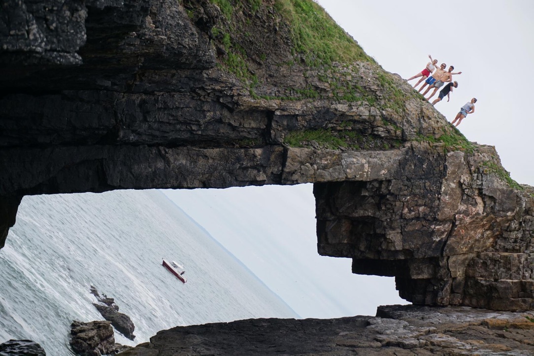 A group standing on the edge of a sea arch, about to jump